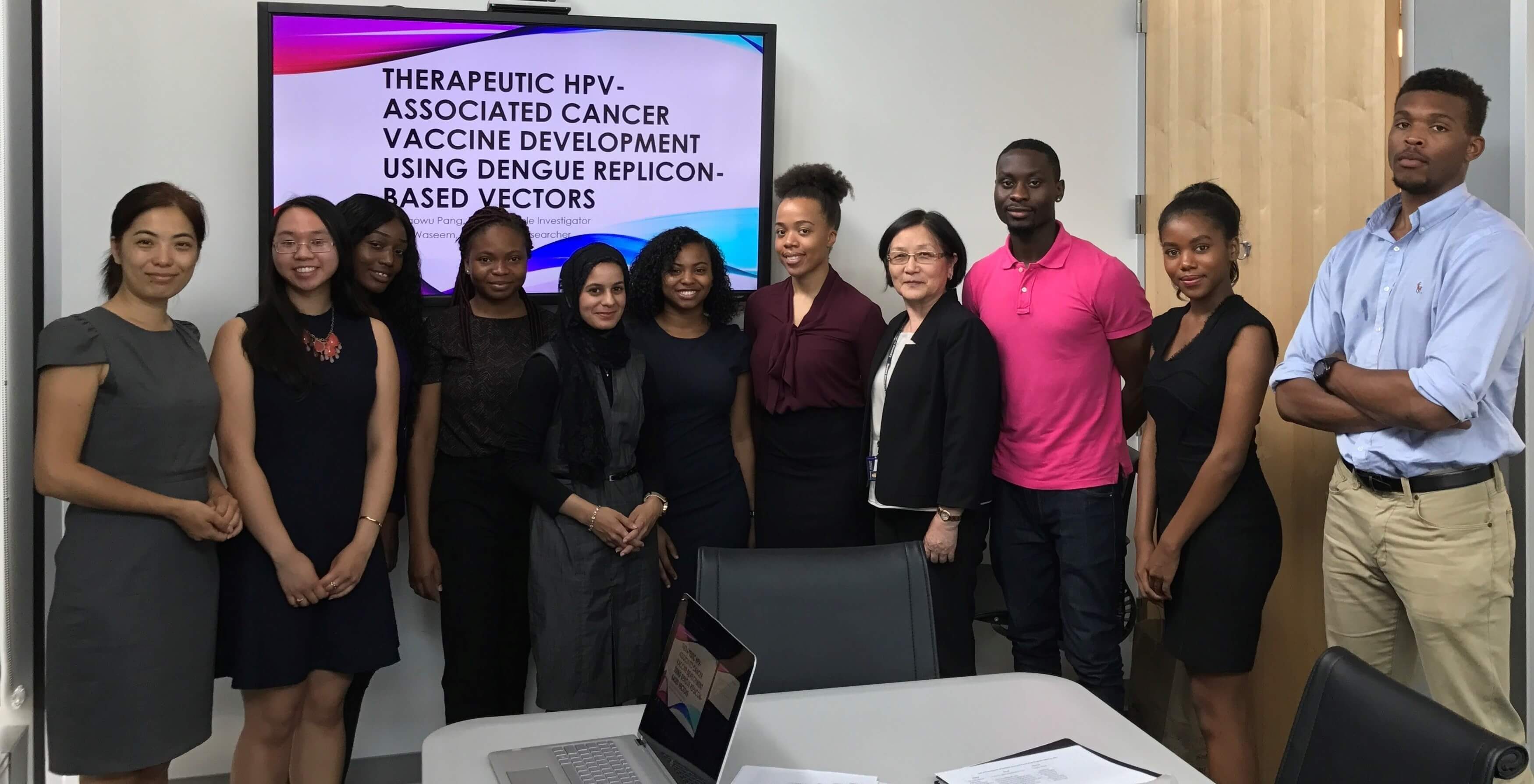 Group of students and professors standing in front of screen with presentation 