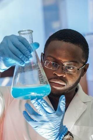 A student holding a triangle beaker with blue liquid in it